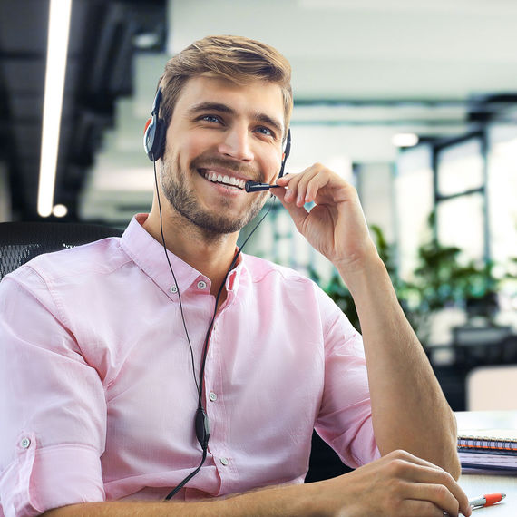 Uomo sorridente con cuffie che lavora in ufficio e tiene in mano un tablet.